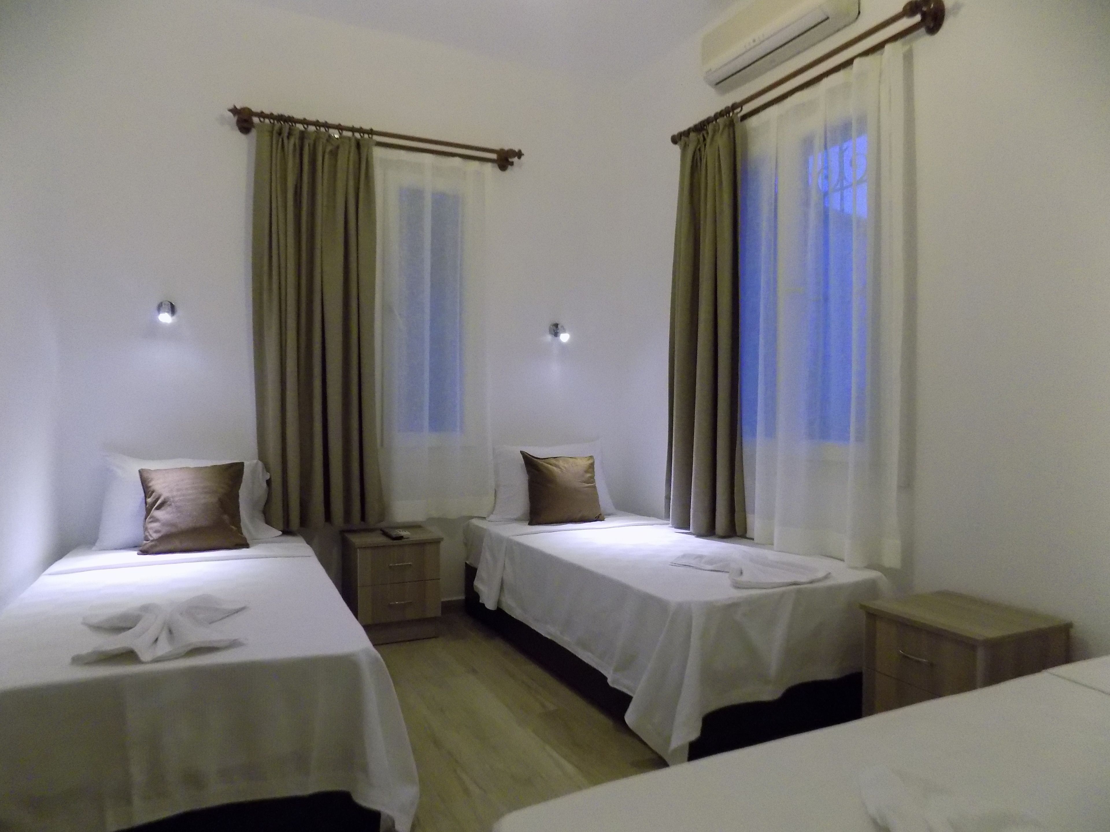 Habitación de hotel con dos camas individuales, una mesita de noche de madera y un equipo de aire acondicionado en la pared.