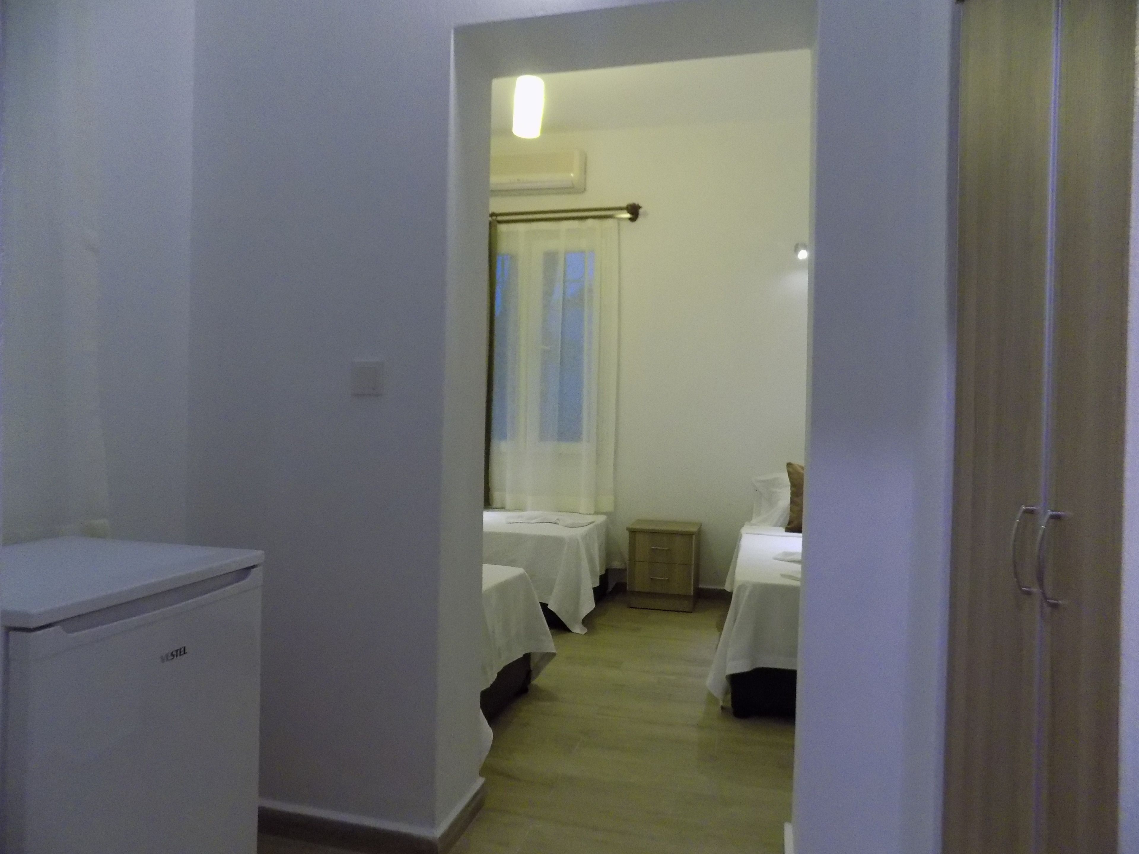 A hotel room with a compact layout, including a bed, a bedside table, and a small kitchenette.