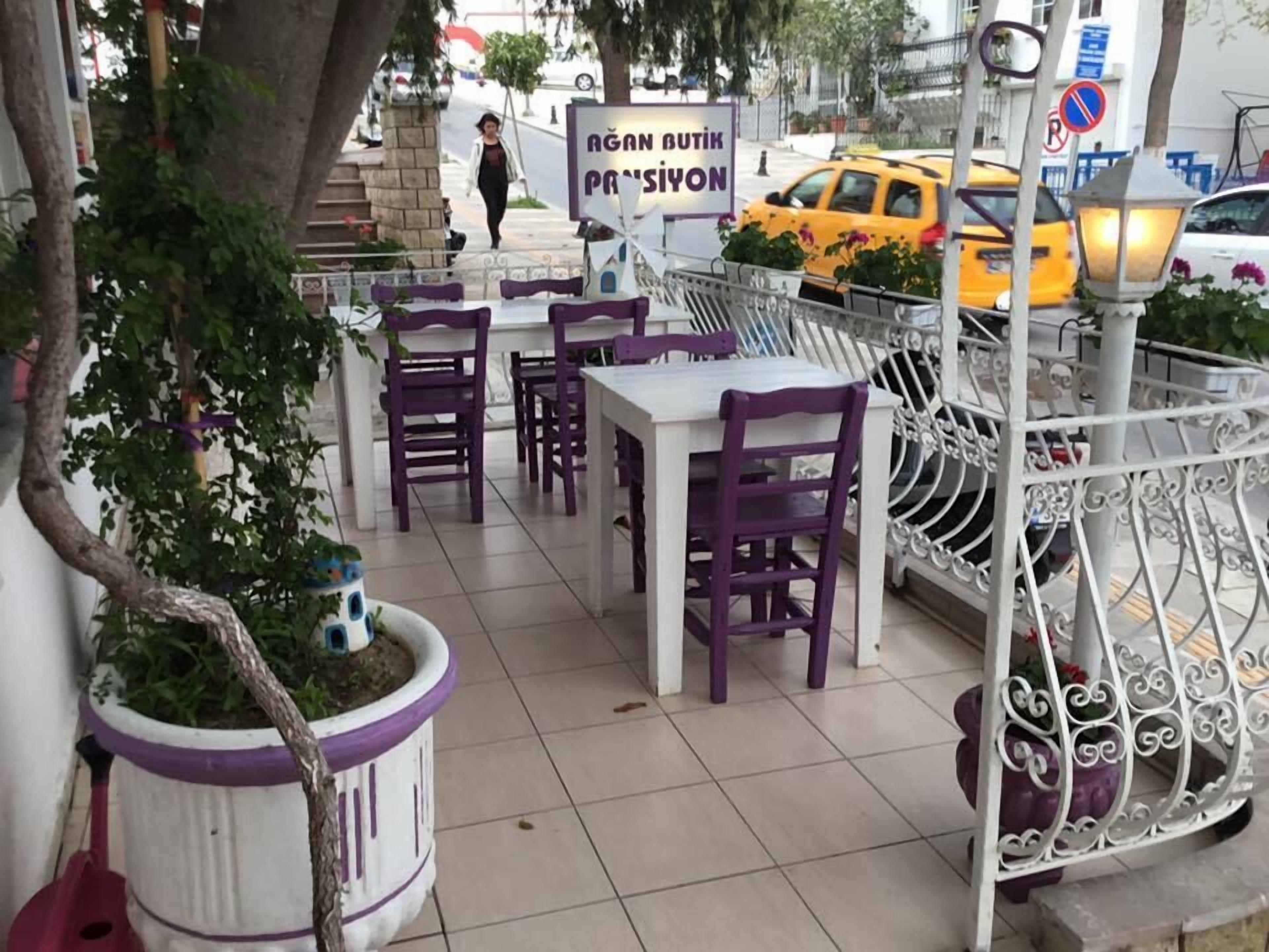 An outdoor seating area with tables and chairs, a potted plant, and a street view with a taxi and a pedestrian.