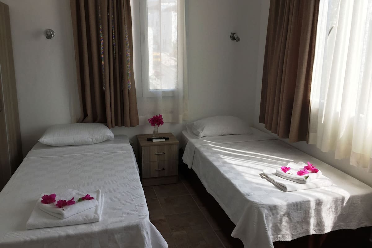 Habitación de hotel con dos camas individuales, una mesita de noche, una ventana con cortinas y un jarrón con flores.