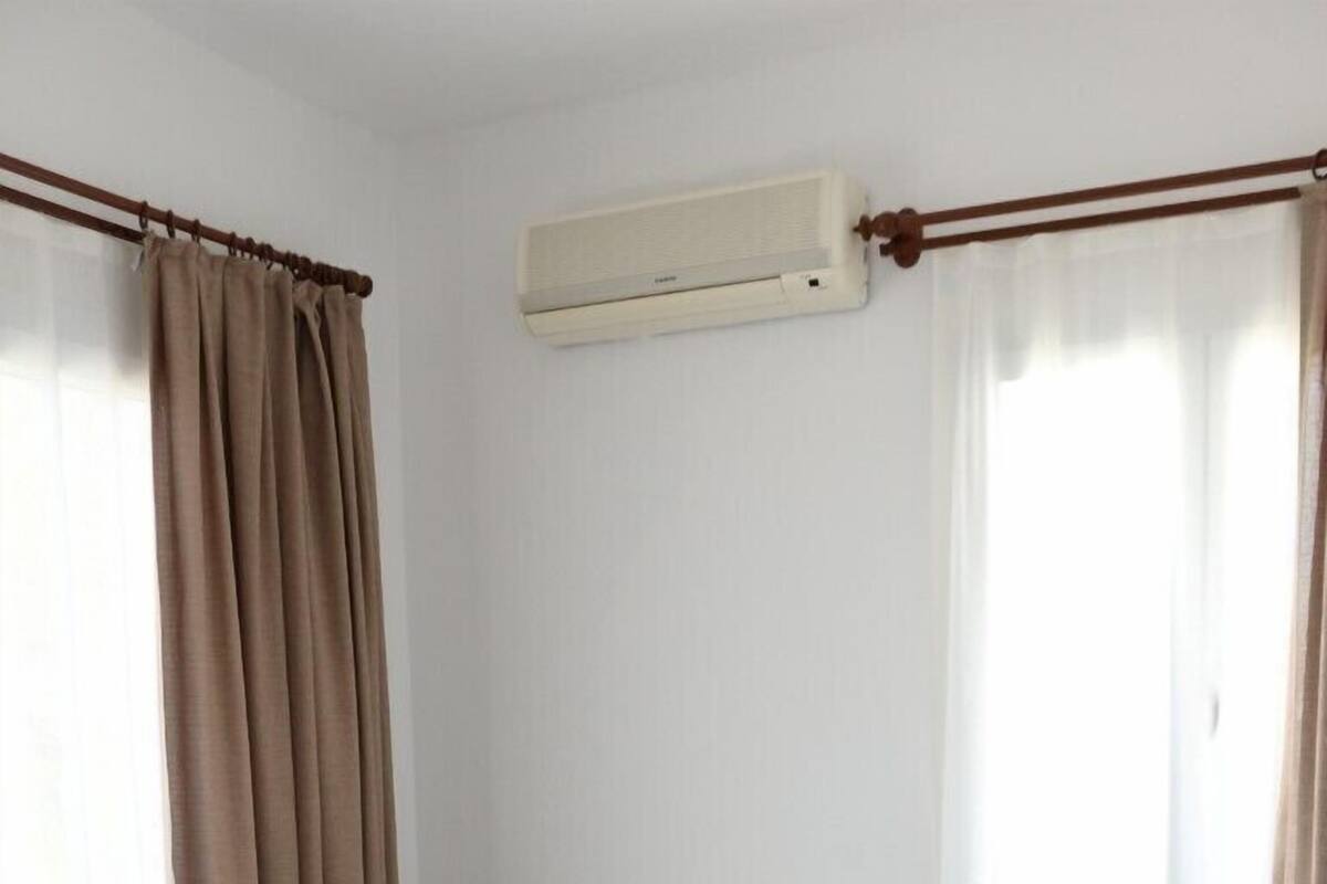 Habitación de hotel con cama, mesita de noche con lámpara y un equipo de aire acondicionado en la pared.