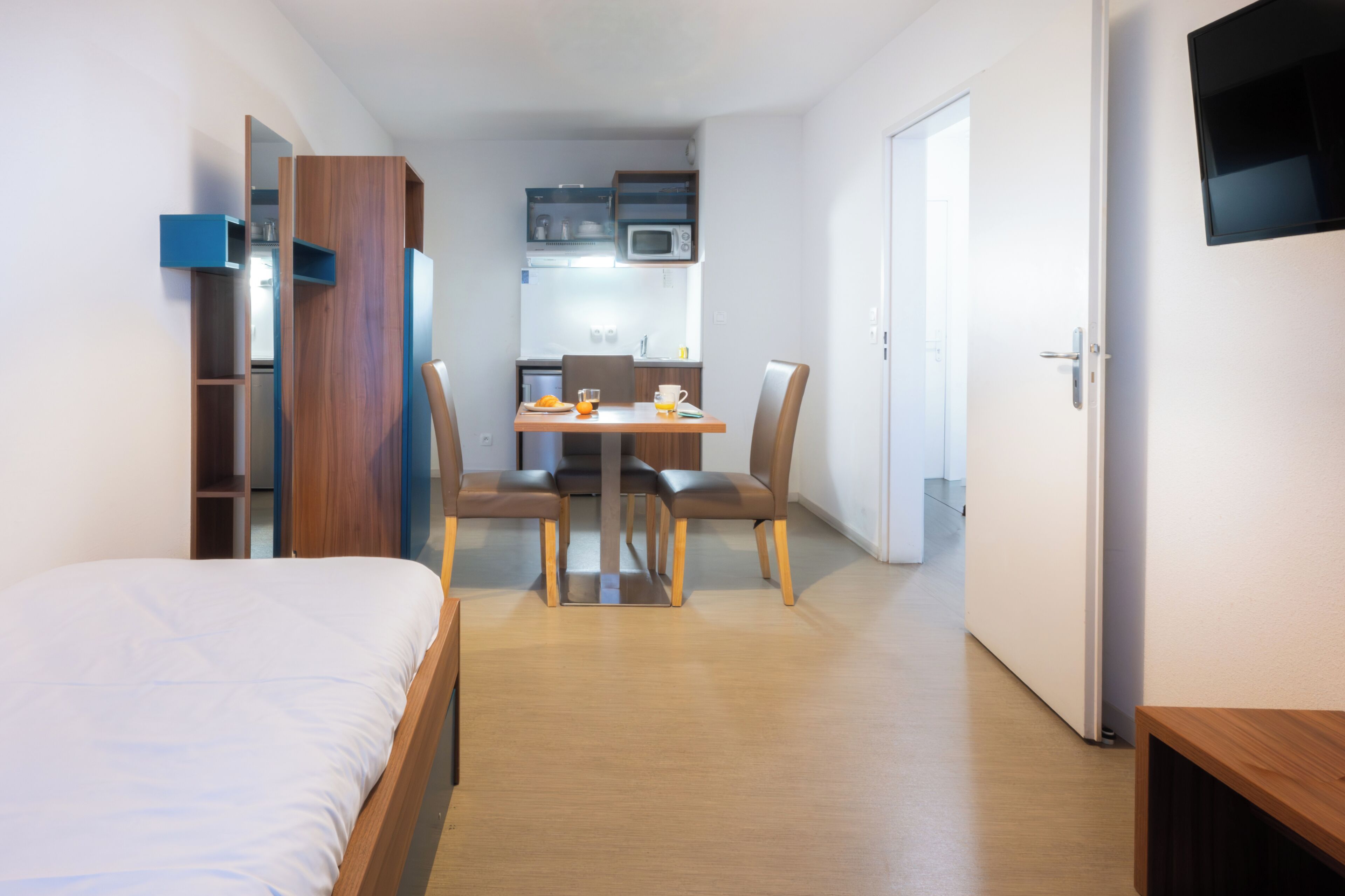 Een knus hotelkamer met een bed, een kleine eettafel met stoelen, een kitchenette en een aan de muur bevestigde televisie.