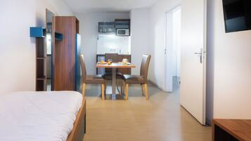 Een knus hotelkamer met een bed, een kleine eettafel met stoelen, een kitchenette en een aan de muur bevestigde televisie.