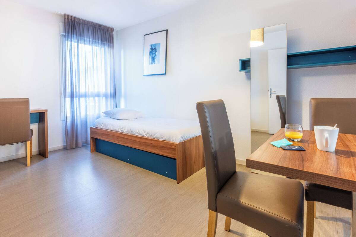 Une chambre d’hôtel moderne avec un lit, une table à manger avec des chaises, un miroir et un tableau au mur.