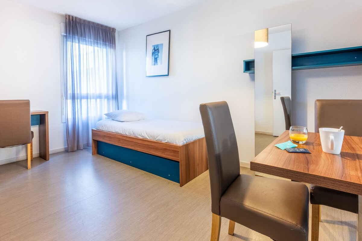Une chambre d’hôtel moderne, équipée d’un lit, d’une table à manger, de chaises, d’un miroir et d’un tableau au mur.
