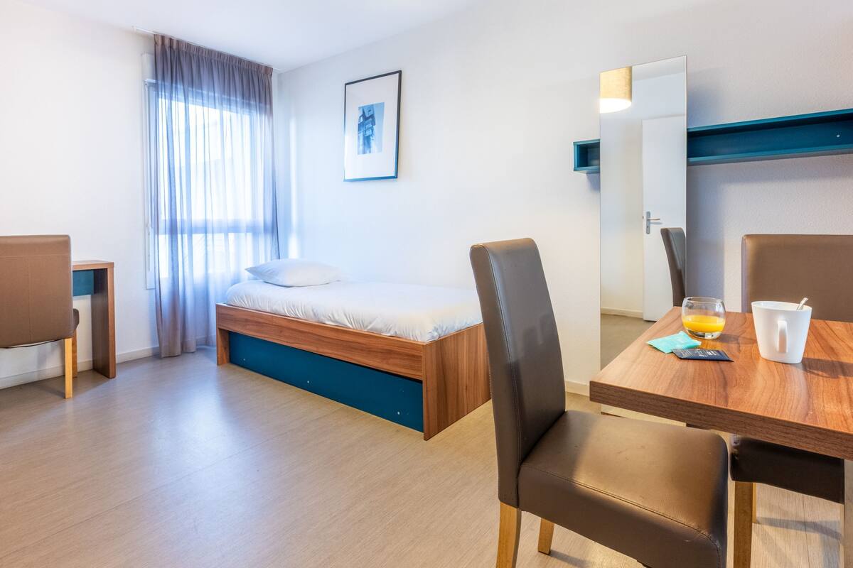 Une chambre d’hôtel moderne, équipée d’un lit, d’une table à manger, de chaises, d’un miroir et d’un tableau au mur.