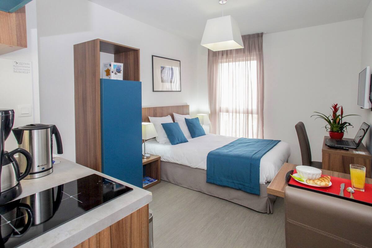 Une chambre d’hôtel comprenant un lit, une table de chevet, un bureau avec un ordinateur portable, une machine à café et un plateau de petit-déjeuner.