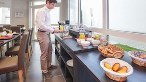 A breakfast bar with various food items and a man preparing food. - Appart'hôtel Odalys City - Orléans Centre (Orléans)