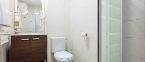 A bathroom with a toilet, vanity, mirror, and shower.