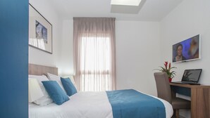 A neatly arranged hotel room with a bed, a desk, a chair, a TV, and a window with curtains. - Appart'hôtel Odalys City - Orléans Centre (Orléans)