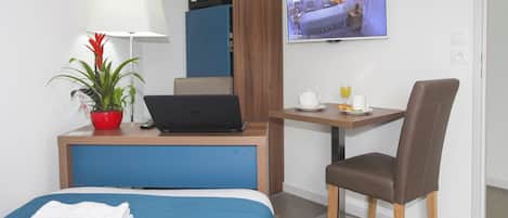 Habitación de hotel con cama, escritorio con una laptop, silla, televisor, planta y mesa con una taza y un vaso.