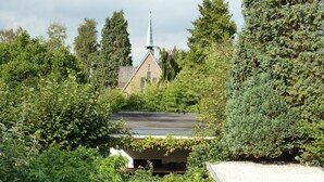 A rooftop garden with a view of a church steeple, surrounded by dense greenery and a gravel path. - Hotel Het Oude Postkantoor (Brummen)