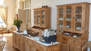 A kitchen with wooden cabinets, a central island with a coffee machine, and a dining area with wicker chairs. - Hotel Het Oude Postkantoor (Brummen)