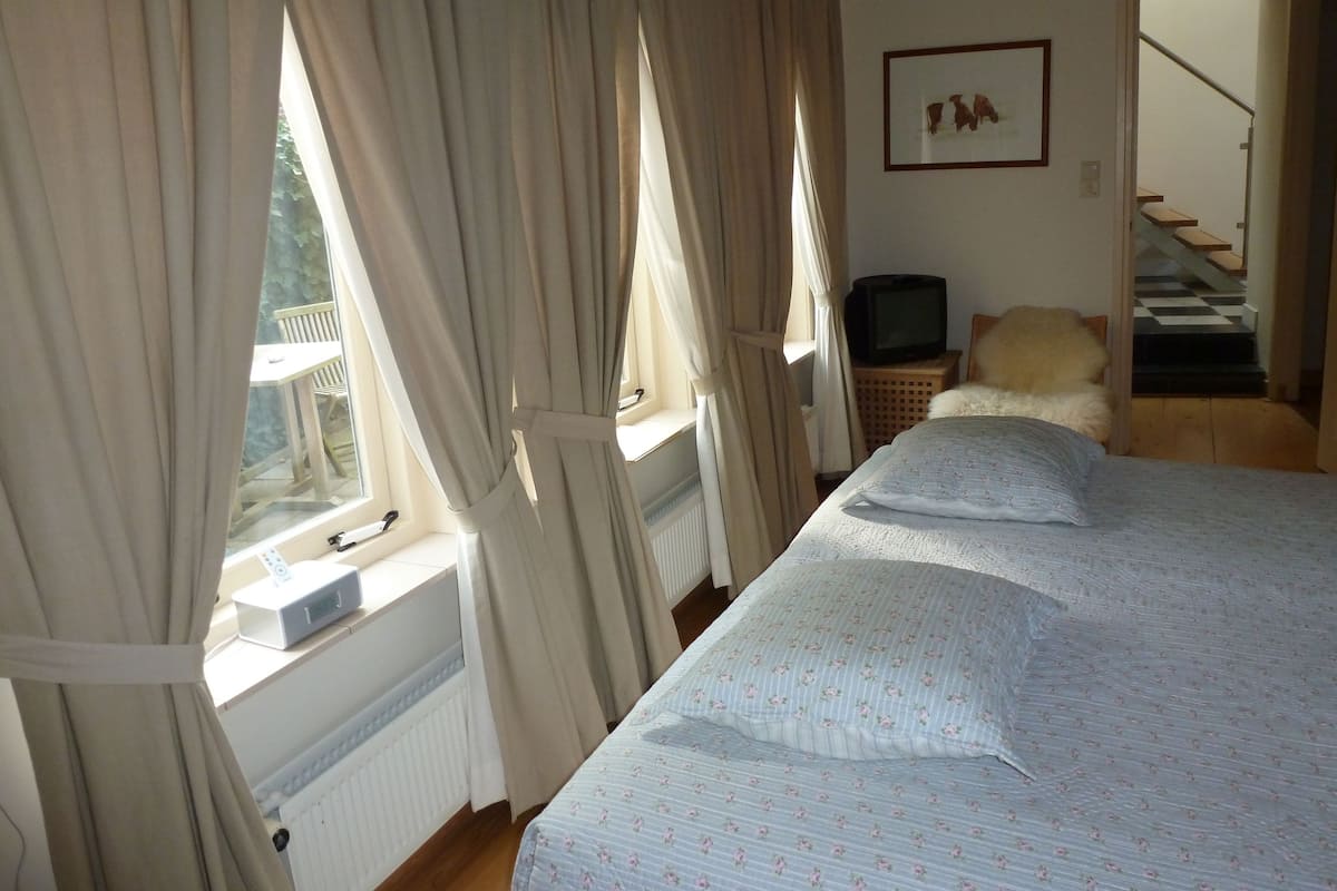 A bedroom with two beds, a TV, a radiator, and a staircase leading to an upper floor.