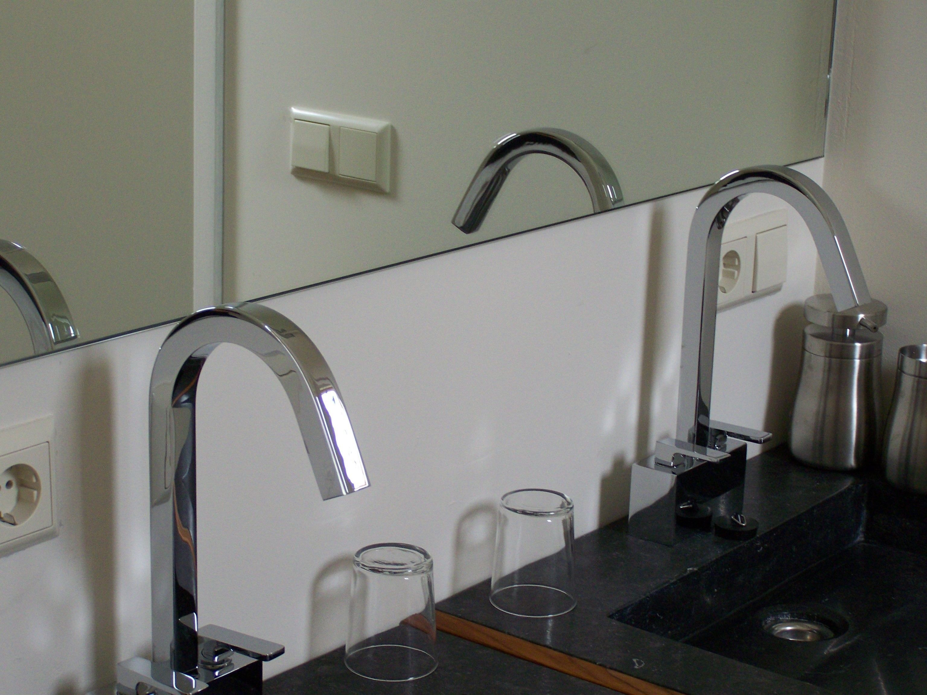 A bathroom with a mirror, a sink, and a faucet. There are two clear glasses on the sink.