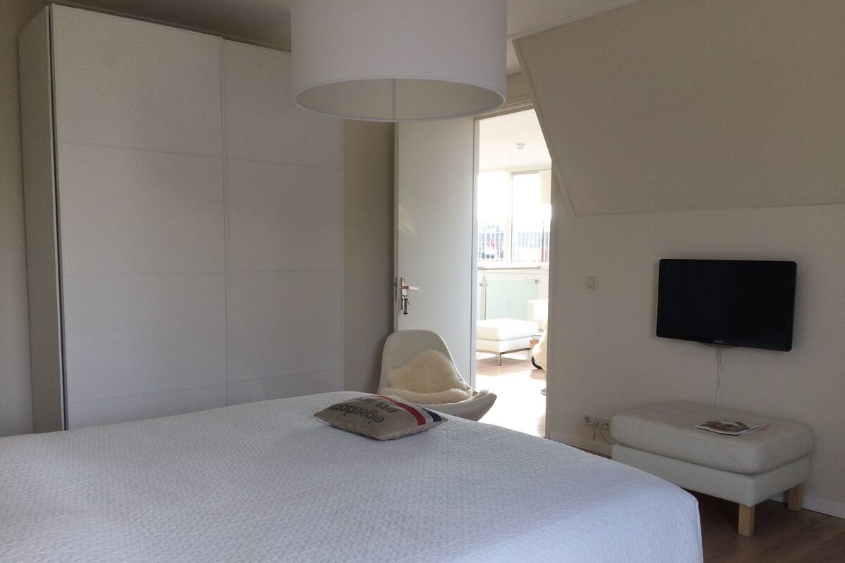 A bedroom with a large bed, a chair, a television, and a wardrobe.