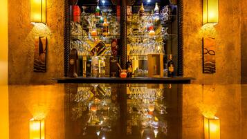 A bar with a polished reflective surface, shelves with various bottles and glasses, and wall-mounted light fixtures.