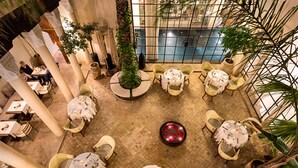 An indoor dining area with round tables, chairs, and potted plants. - Palais Khum (Marrakech)