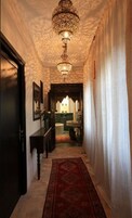 Un corridoio con tappeto decorato, un lampadario e vista su una stanza con tappeto verde e un lavandino.