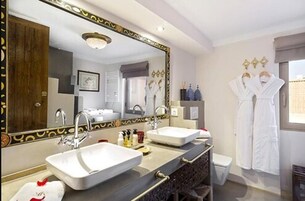 A hotel bathroom with two sinks, a large mirror, and a vanity with a dark patterned cabinet.