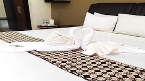 Een net opgemaakt bed met witte lakens, een bruin decoratief loper en twee witte handdoeken gevouwen tot zwanen.