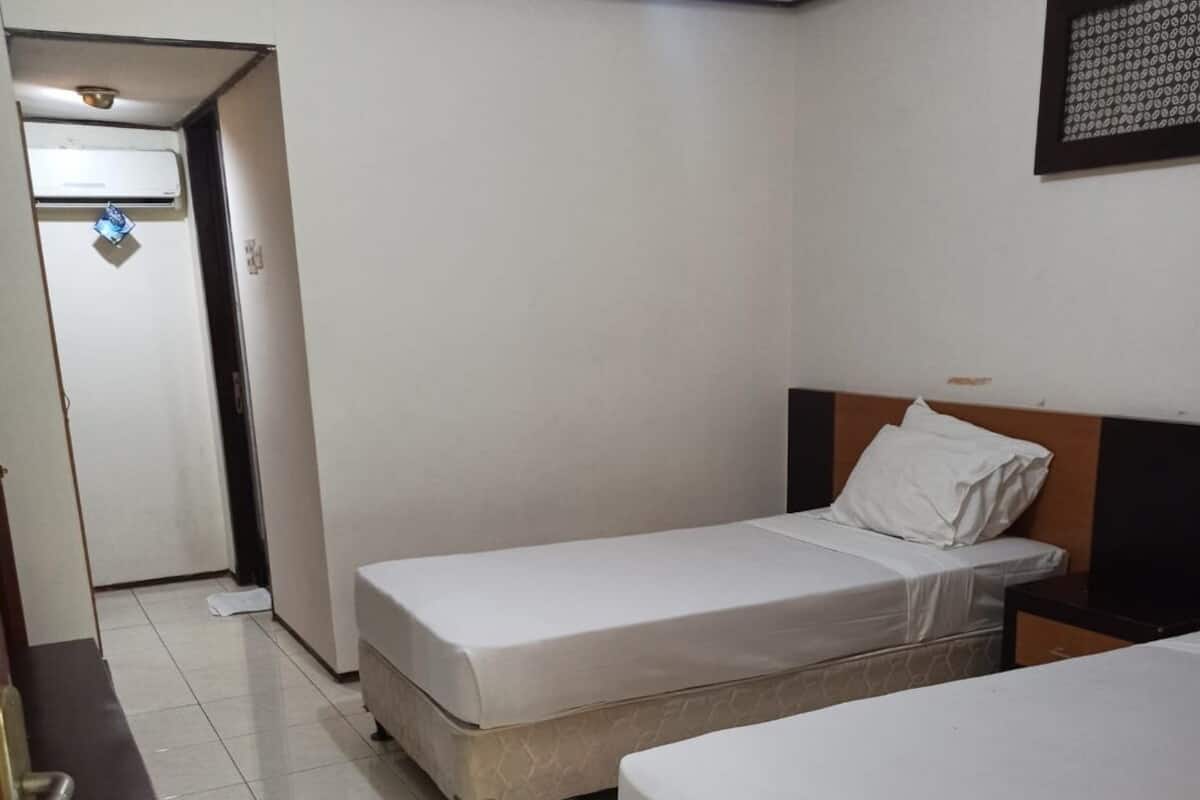 Ein Zimmer mit zwei Betten, einem Schreibtisch und einer Tür zu einem weiteren Raum.