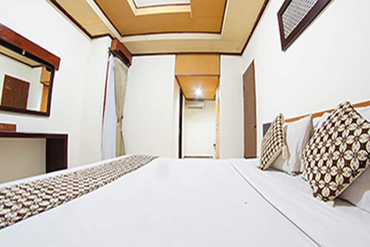 Ein Hotelzimmer mit einem großen Bett, einem Nachttisch, einem Spiegel und einer Tür zu einem weiteren Raum.