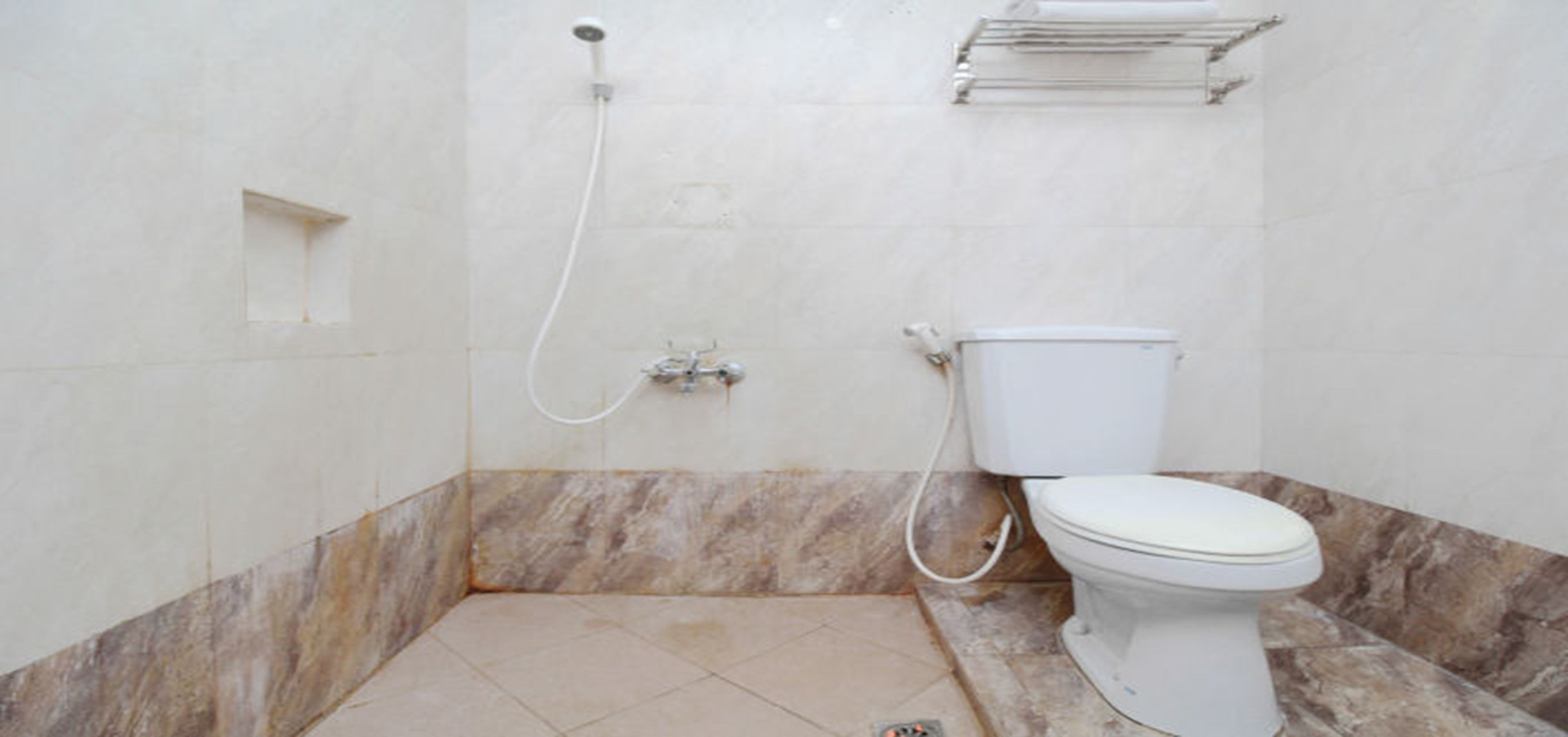 A bathroom with a toilet, a shower, and a marble-tiled floor.