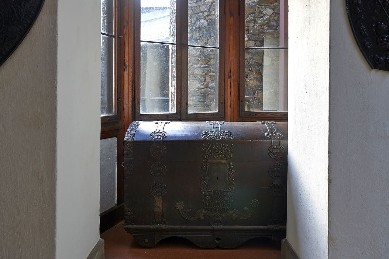 A corner room with a wooden chest, a stone wall, and a window with multiple panes.