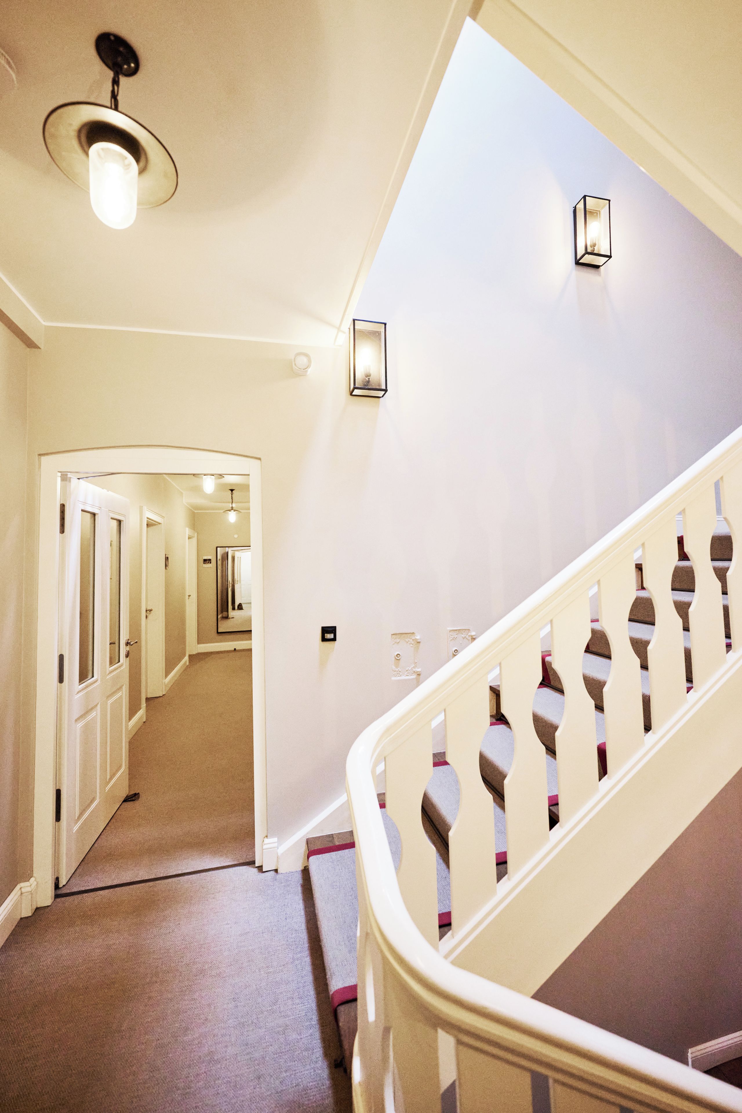 A staircase with a white railing and a carpeted floor leading to a hallway with doors.