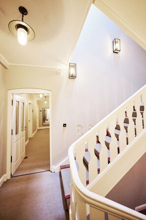 A staircase with a white railing and a carpeted floor leading to a hallway with doors. - Hotel Burg Reichenstein (Trechtingshausen)