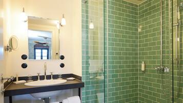 A bathroom with a glass-enclosed shower, a sink with a mirror, and a tiled floor.