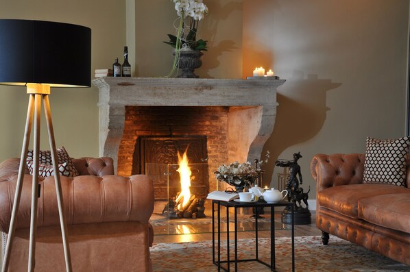 Un salón acogedor con chimenea, sofás de cuero, una lámpara de pie y una mesa con objetos decorativos.
