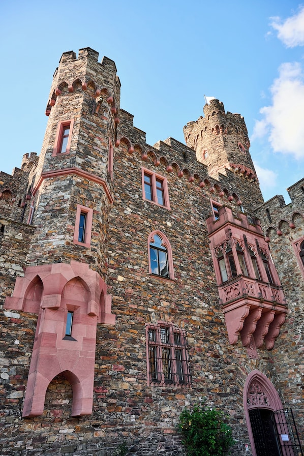 A historic stone castle with multiple towers, arched windows, and a prominent entrance. - Hotel Burg Reichenstein (Trechtingshausen)