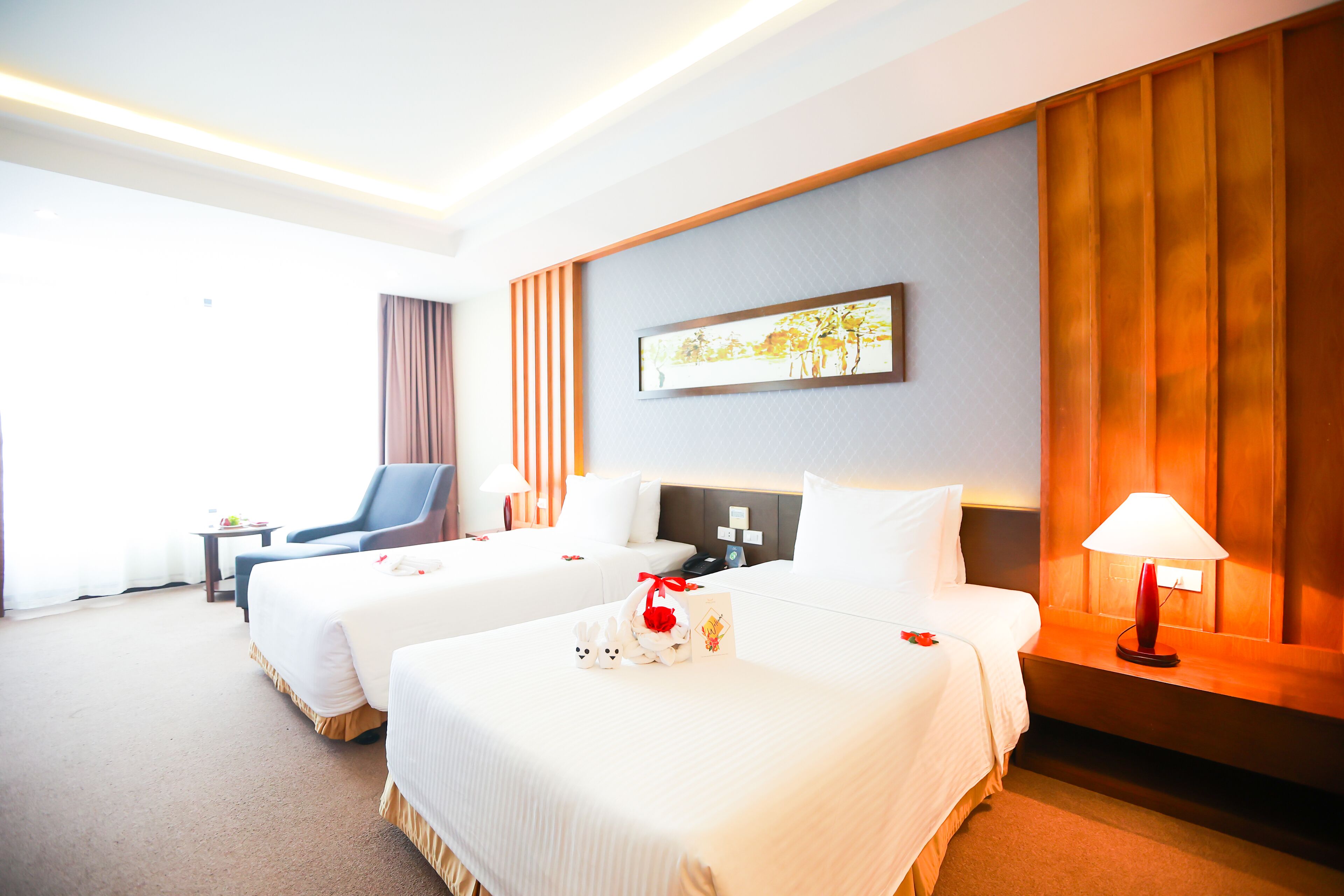 Une chambre d’hôtel avec deux lits, un bureau, une chaise et une table de chevet avec une lampe.