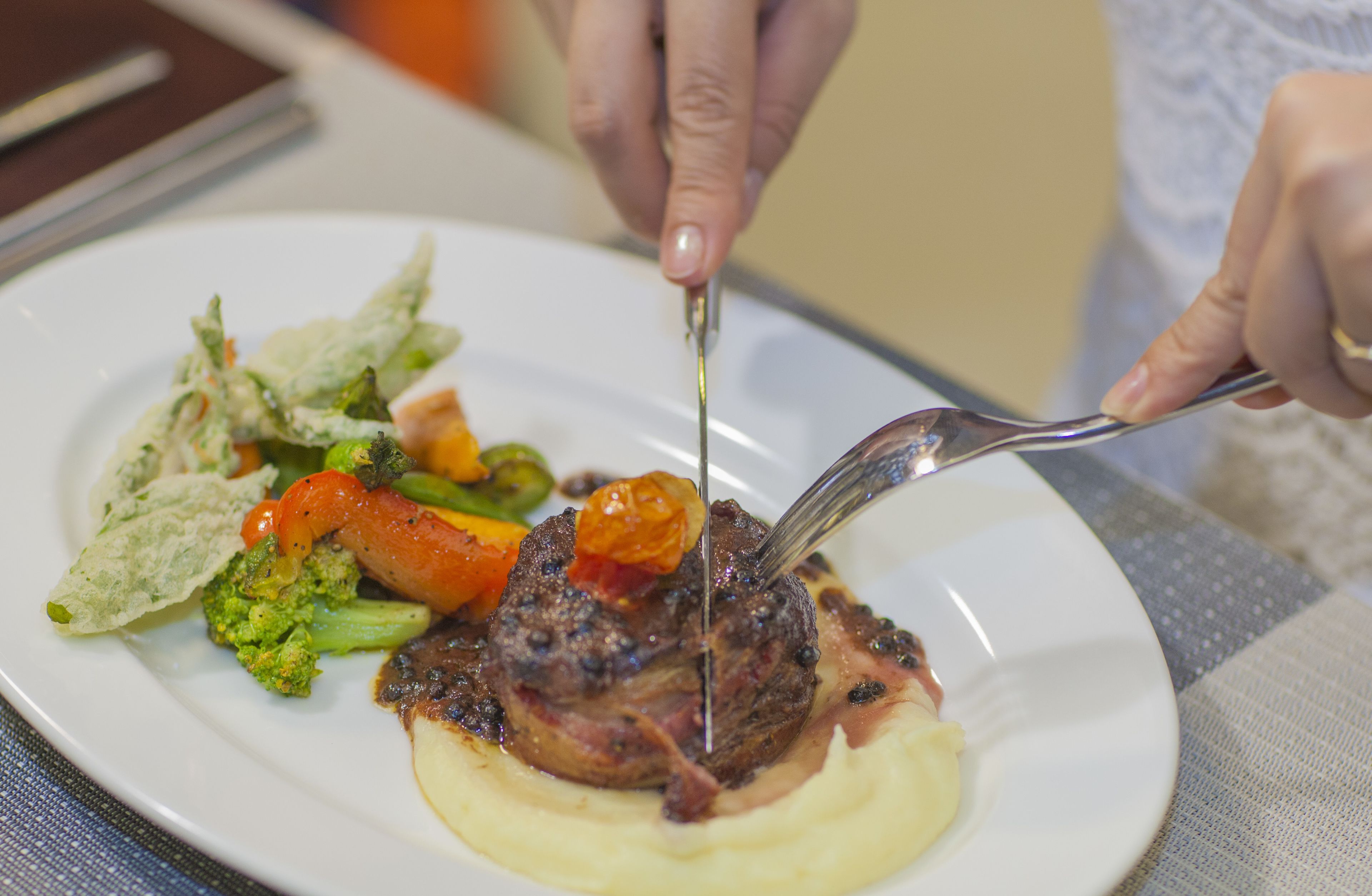 A person cutting a steak with vegetables on a plate.