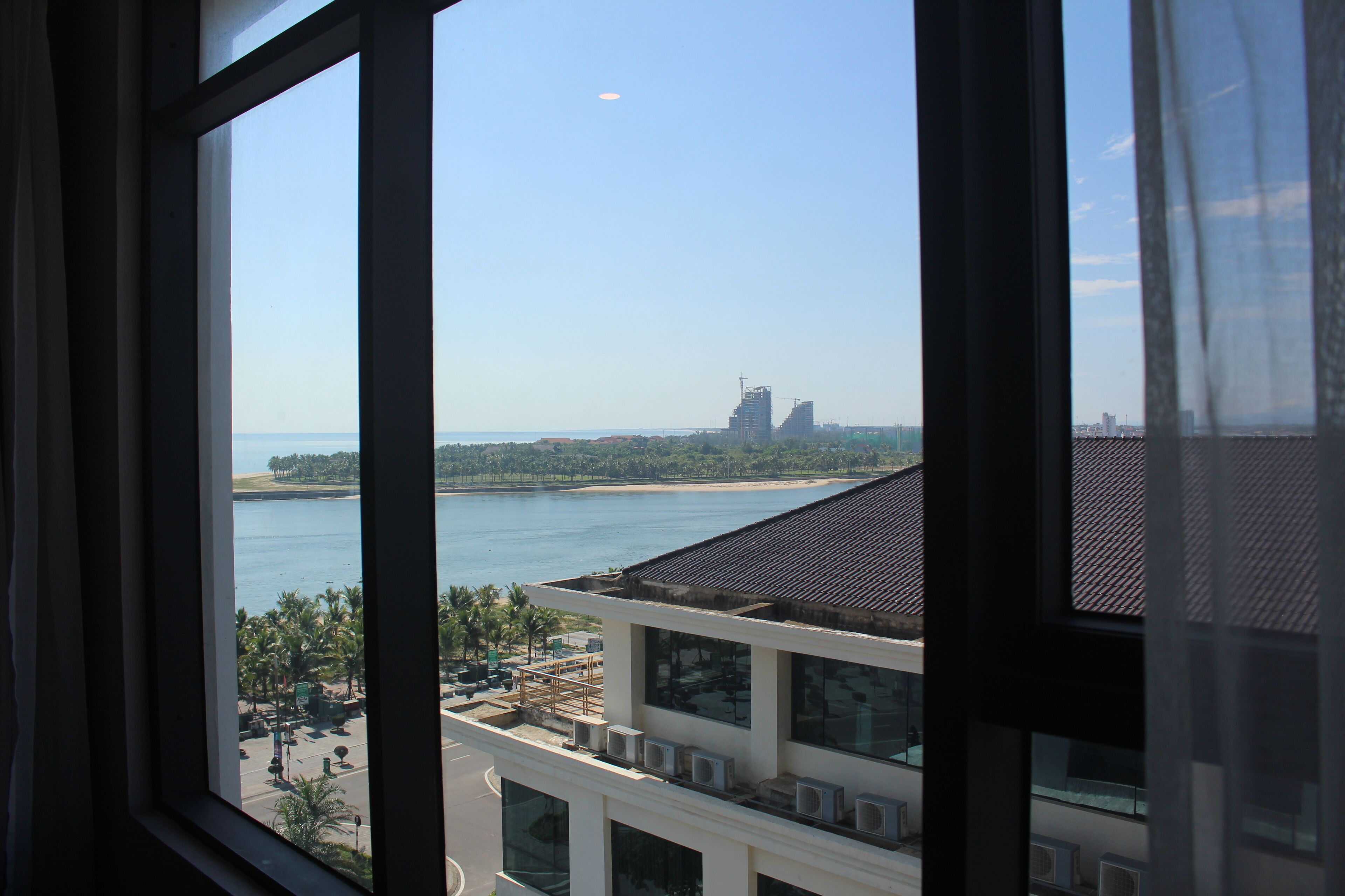 Vista dalla finestra su una zona costiera con edifici, una spiaggia e cielo sereno.
