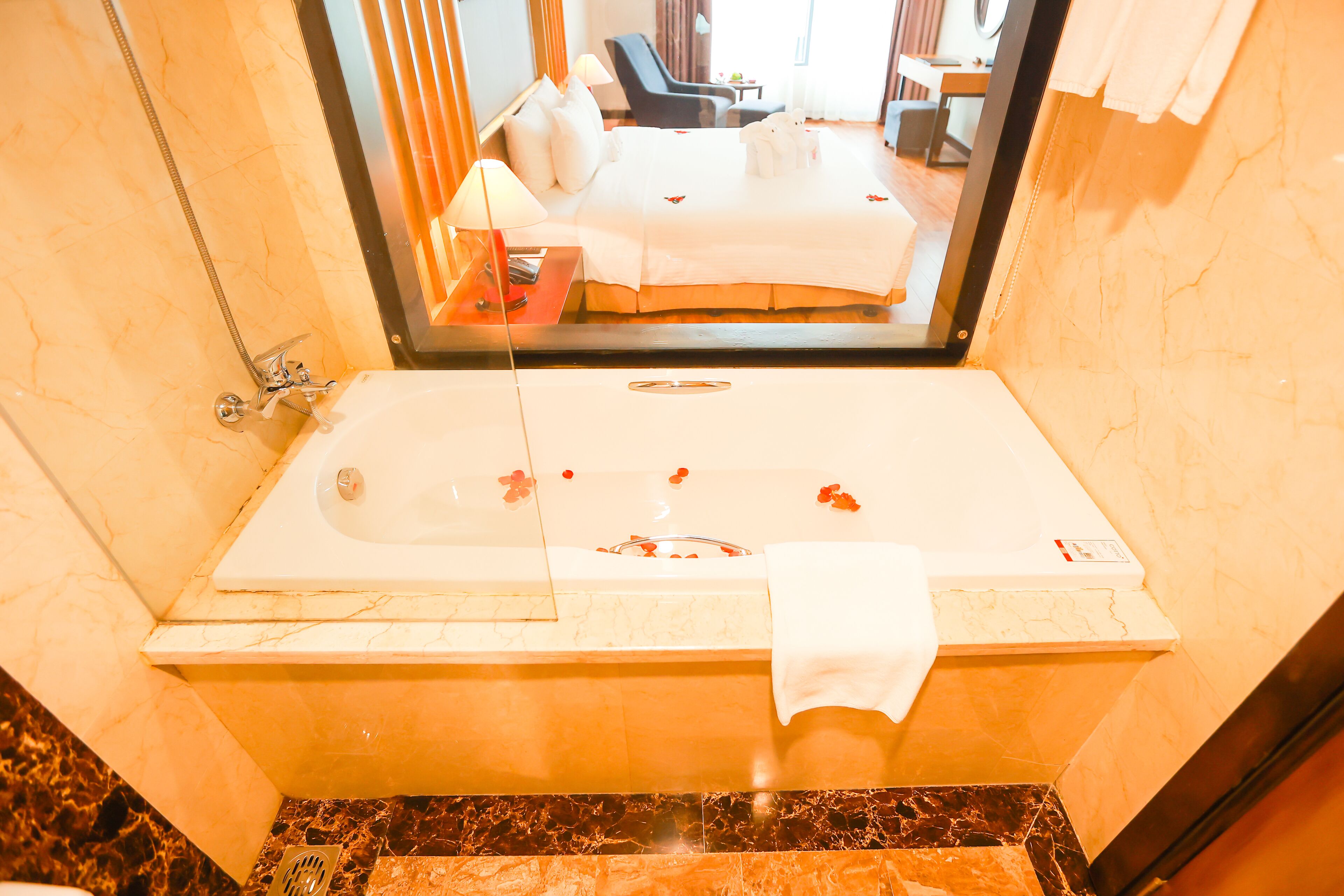 Een badkamer met een bad, een douche en een spiegel die een slaapkamer met een bed en een stoel weerkaatst.