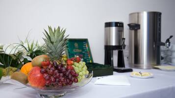 A fruit bowl on a table with a coffee maker and a thermos in the background.