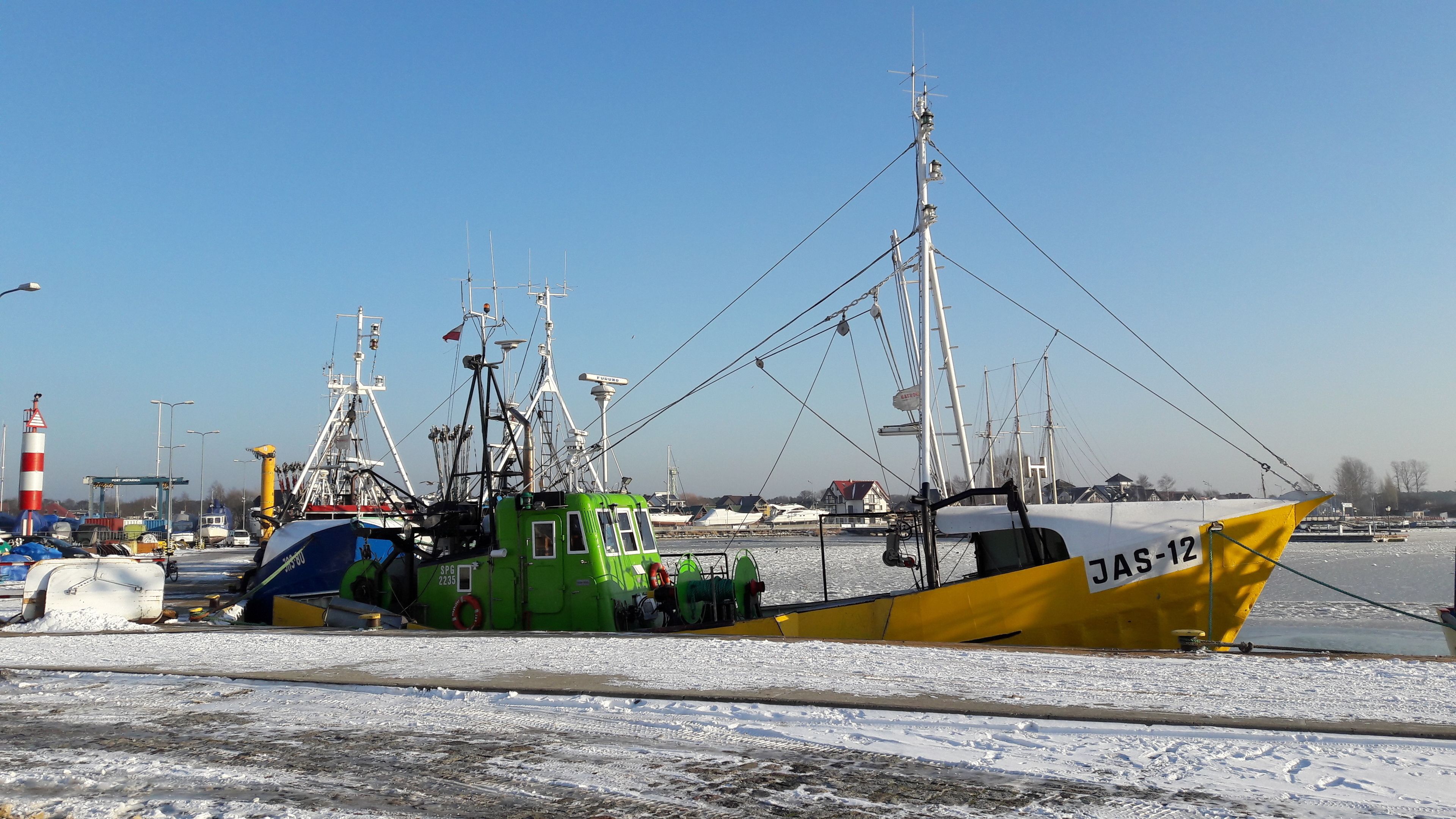 Un port amb vaixells pesquers amarrats, un far i un cel serè.