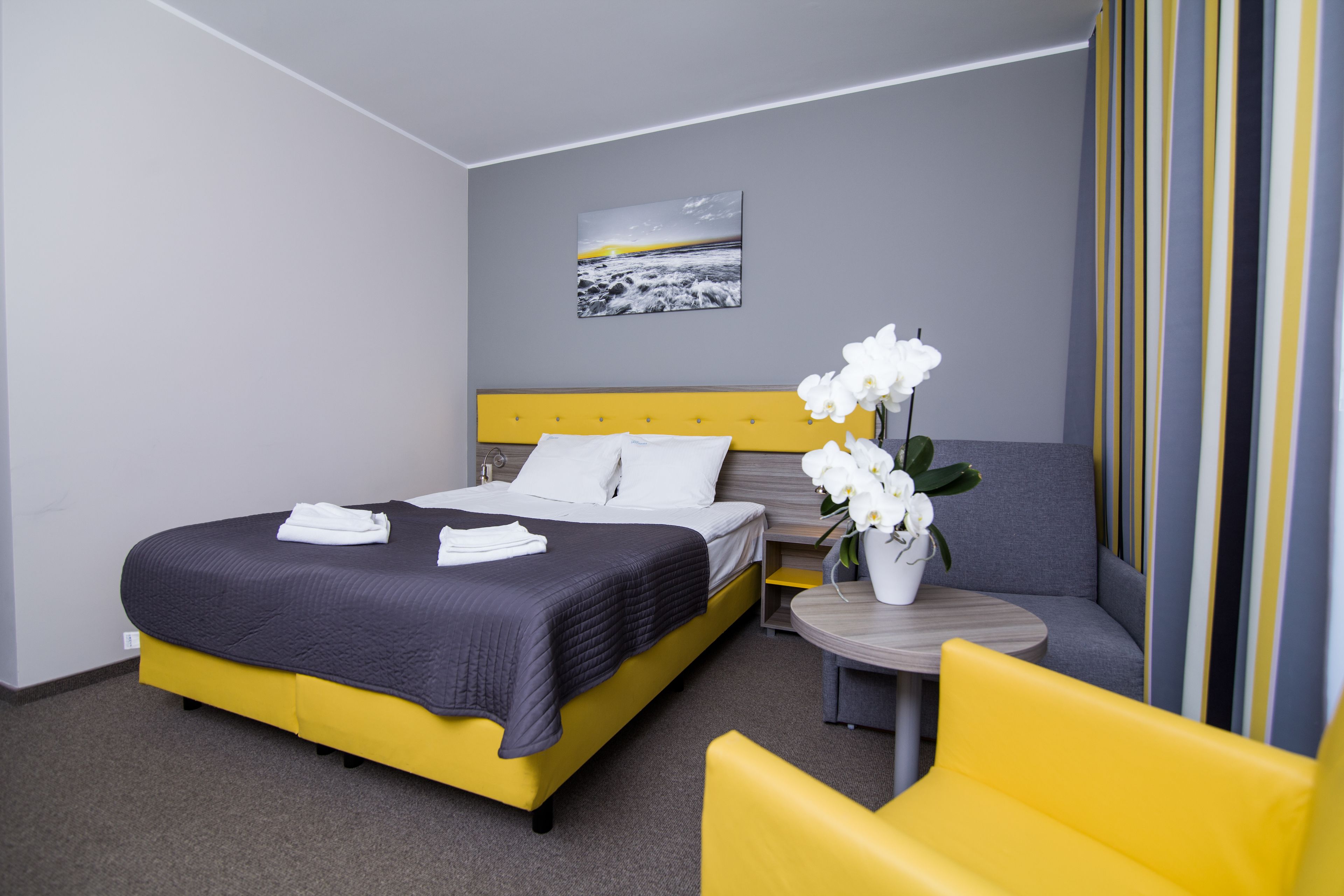 Hotellihuone, jossa on sänky, pieni pöytä maljakko täynnä kukkia ja sohva.