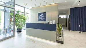 A modern hotel reception desk with a logo, potted plants, and a view of the outdoors. - Hotel Jastarnia (Jastarnia)