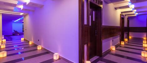 Un pasillo de hotel con diseño moderno, que presenta una puerta de madera, un banco y varios abanicos de luz pequeños e igualmente iluminados.