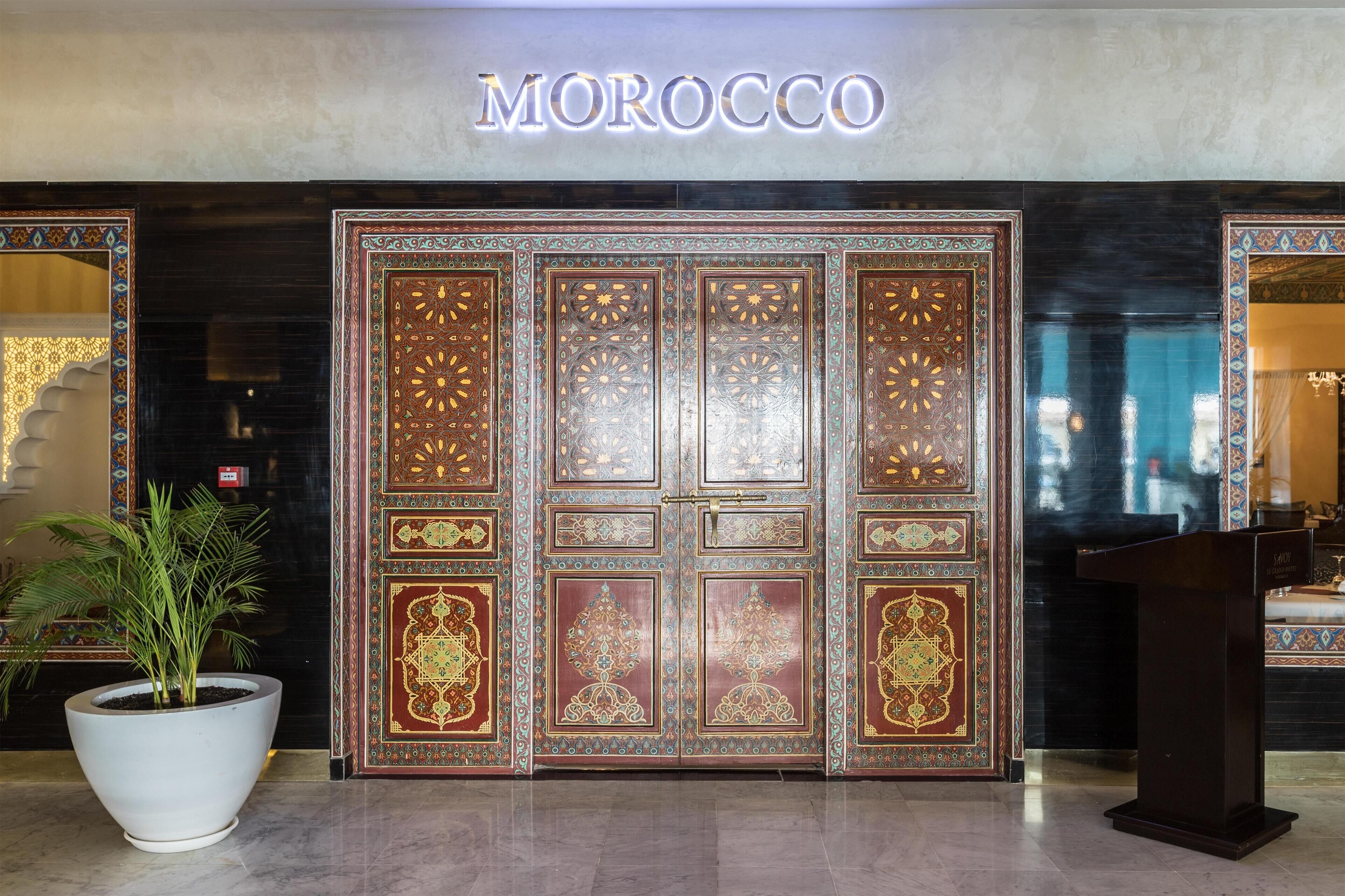 A Moroccan-themed entrance with ornate doors, a potted plant, and a sign above.