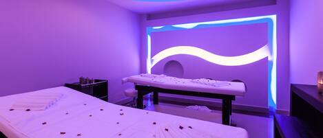 Una stanza per trattamenti benessere con lettino da massaggio, asciugamani e una parete decorata con luci.