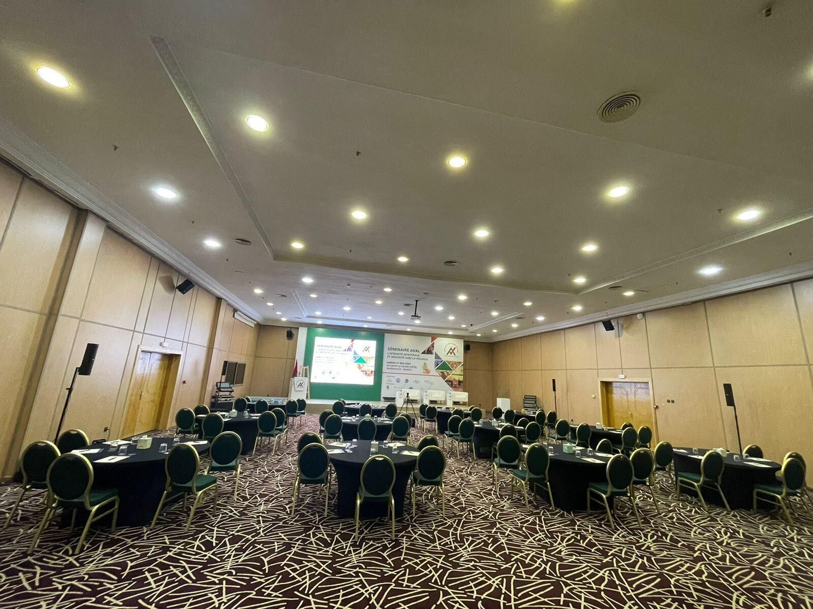 A conference room with multiple tables and chairs, a projector screen, and a carpeted floor.