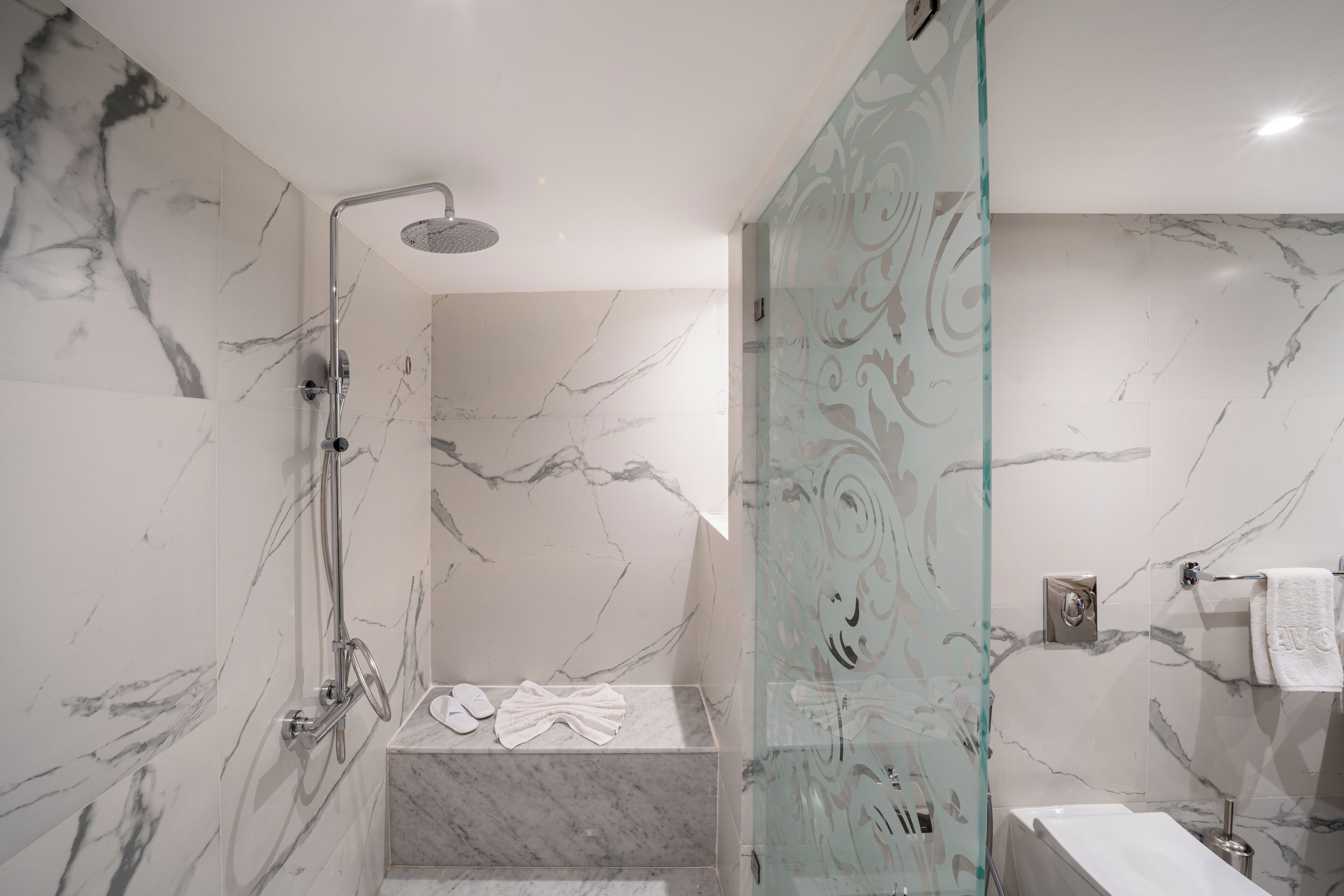 A modern bathroom with marble walls, a glass shower enclosure, a bathtub, and a toilet.