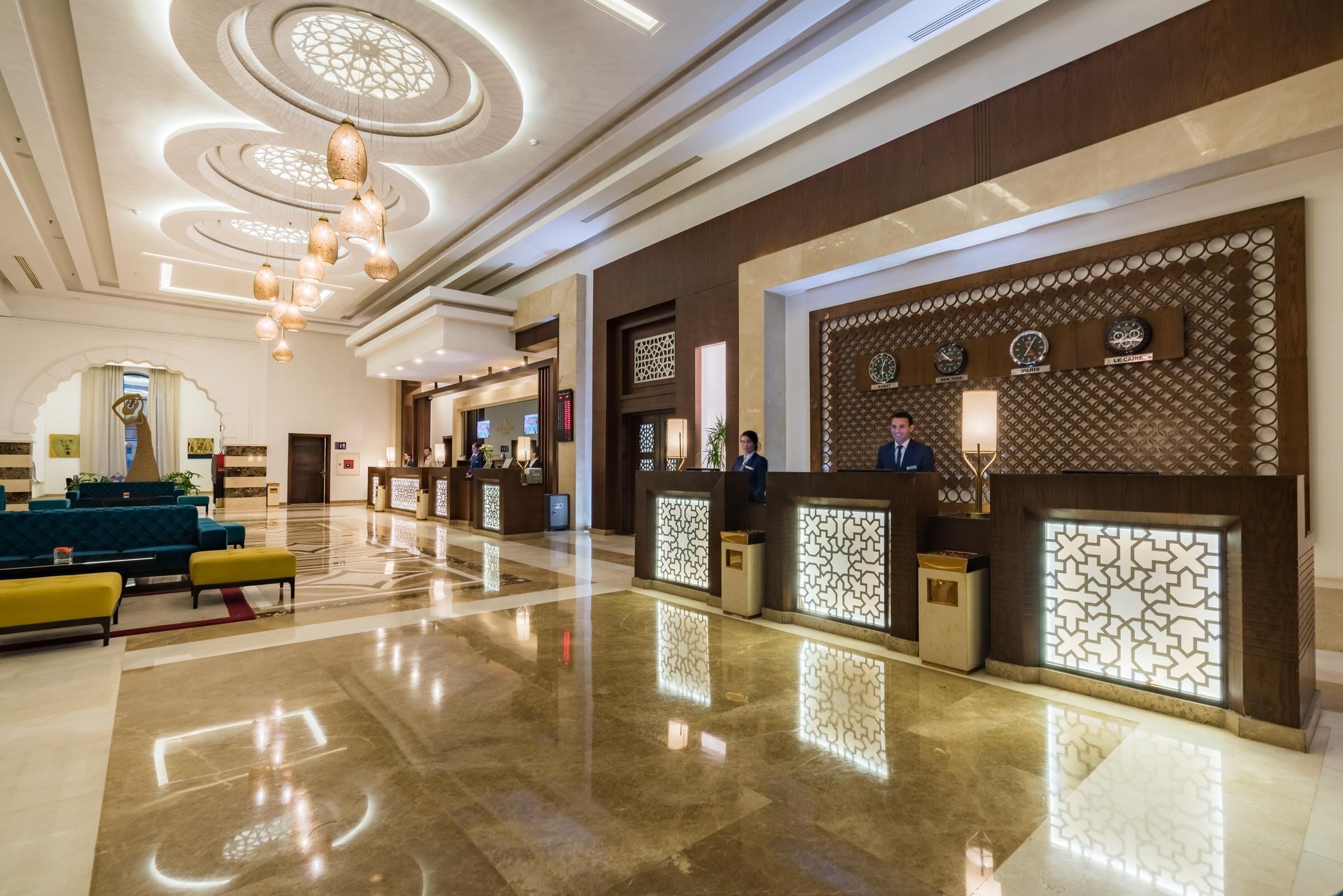 A hotel lobby with a reception desk, seating area, and decorative lighting.
