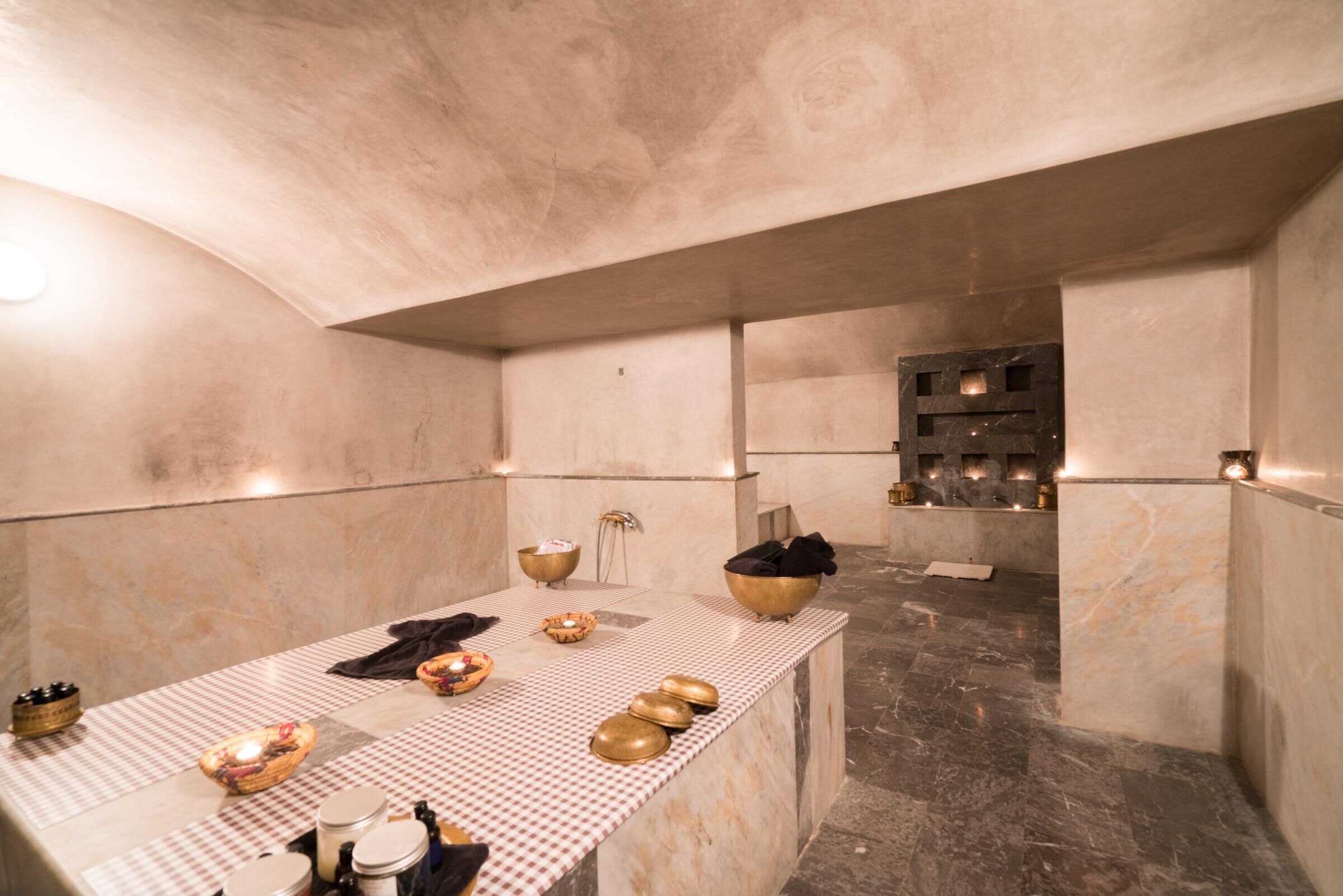 Une salle de bains moderne et minimaliste, avec un tapis de sol à carreaux, des murs en marbre et un espace lavabo central agrémenté de divers produits de toilette.