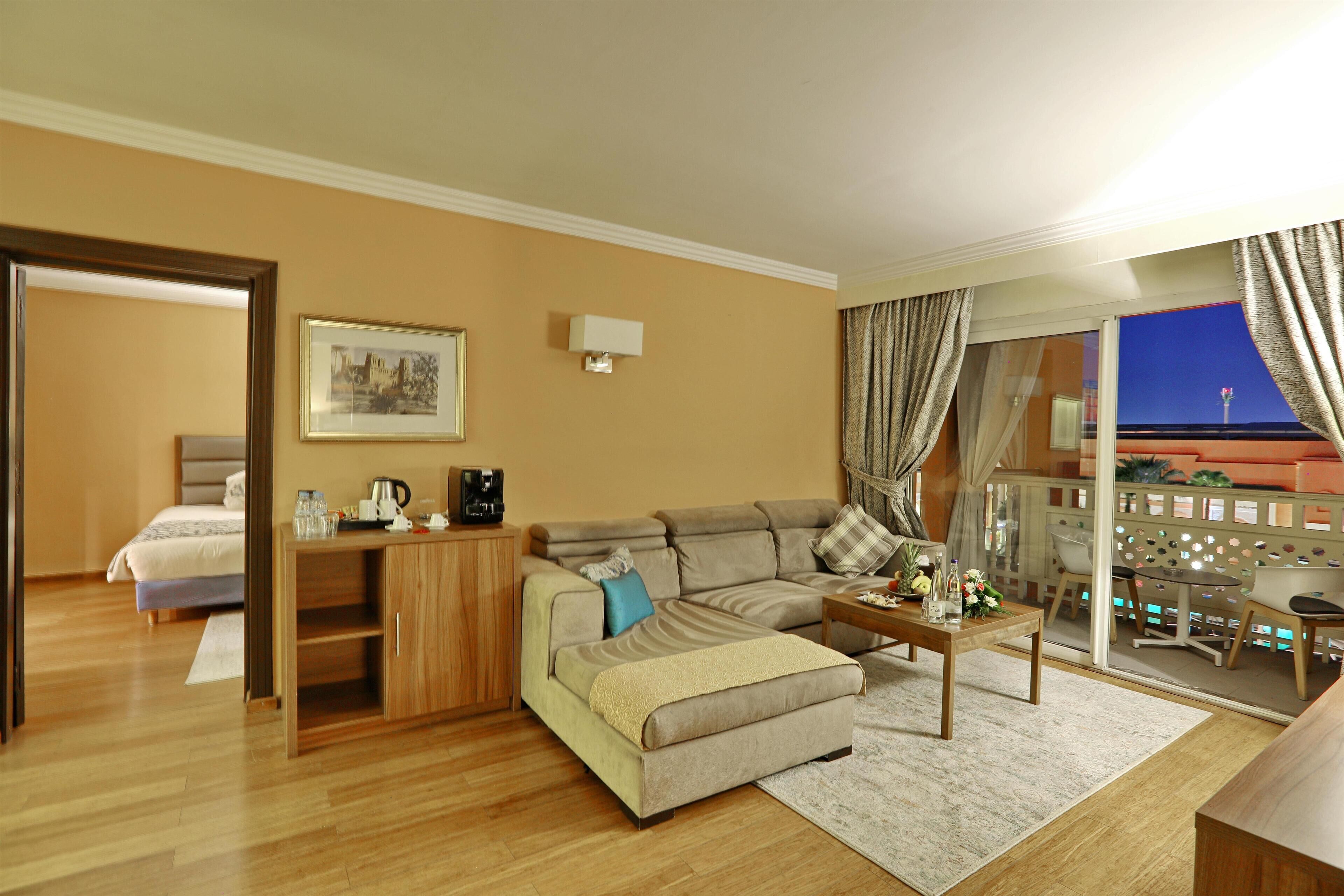 Habitación de hotel con sofá, reposapiés, mesa de centro y vista nocturna de la ciudad.